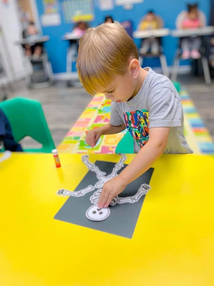 Child assembling a paper skeleton craft on a yellow table