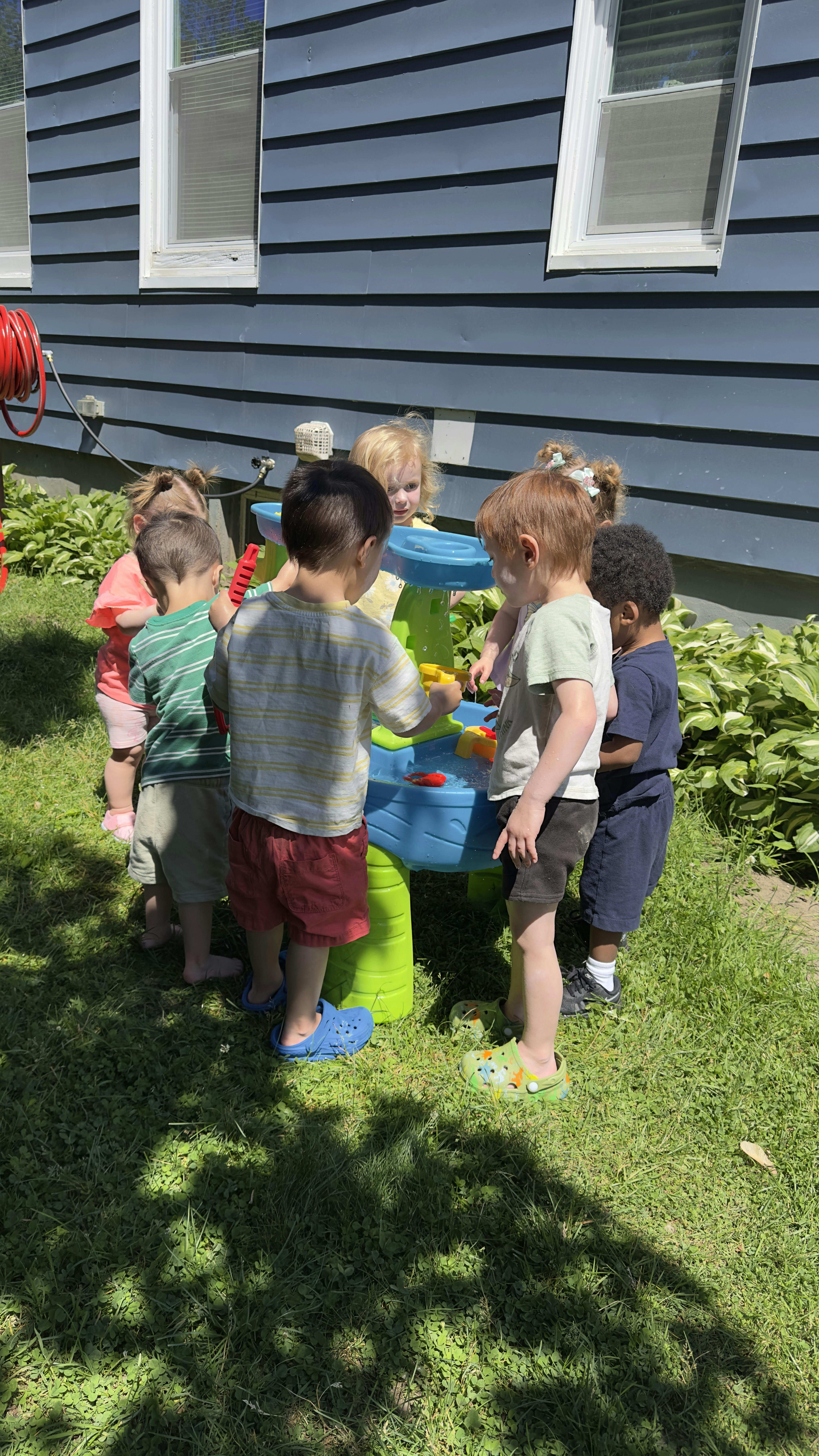 Group of children playing together at a water table in a grassy yard