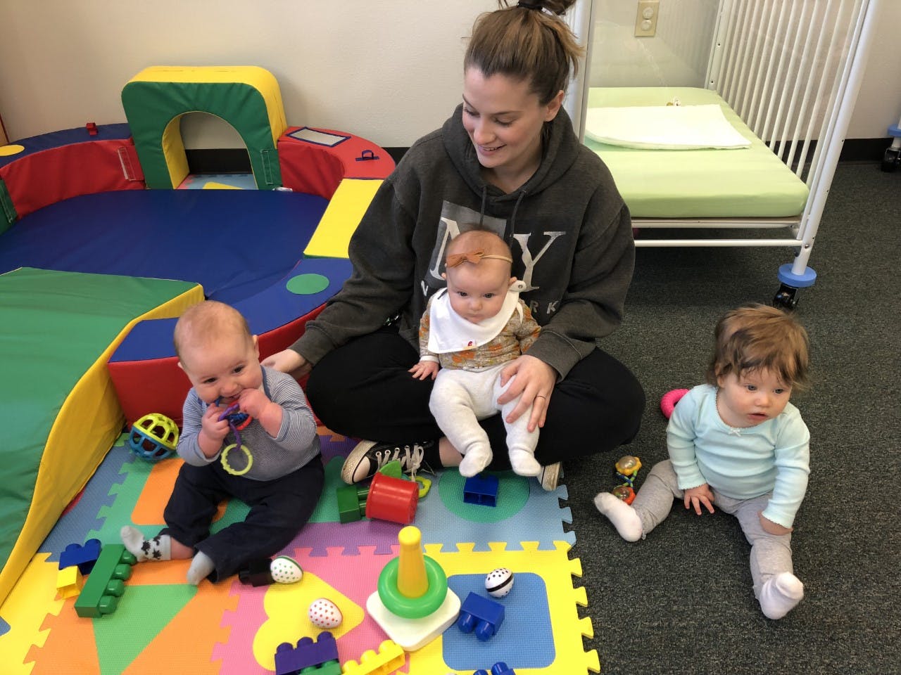 Person sitting on floor with three babies in a play area