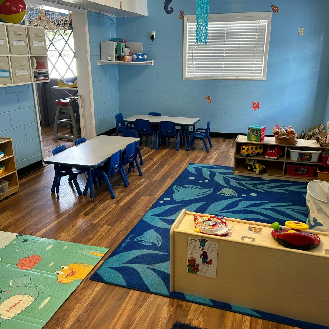 Classroom with small tables and chairs, blue rug, and toys