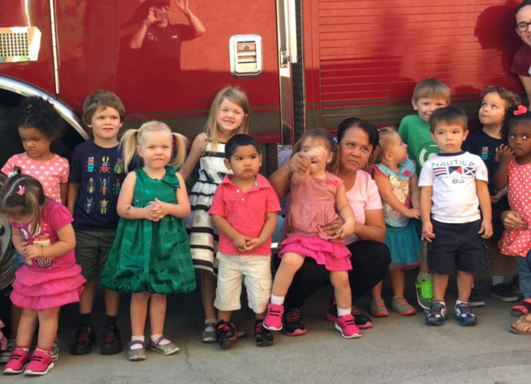 Group of children and an adult posing in front of a red vehicle