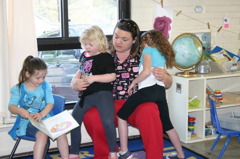 Adult person with two children on lap, another child reading a book