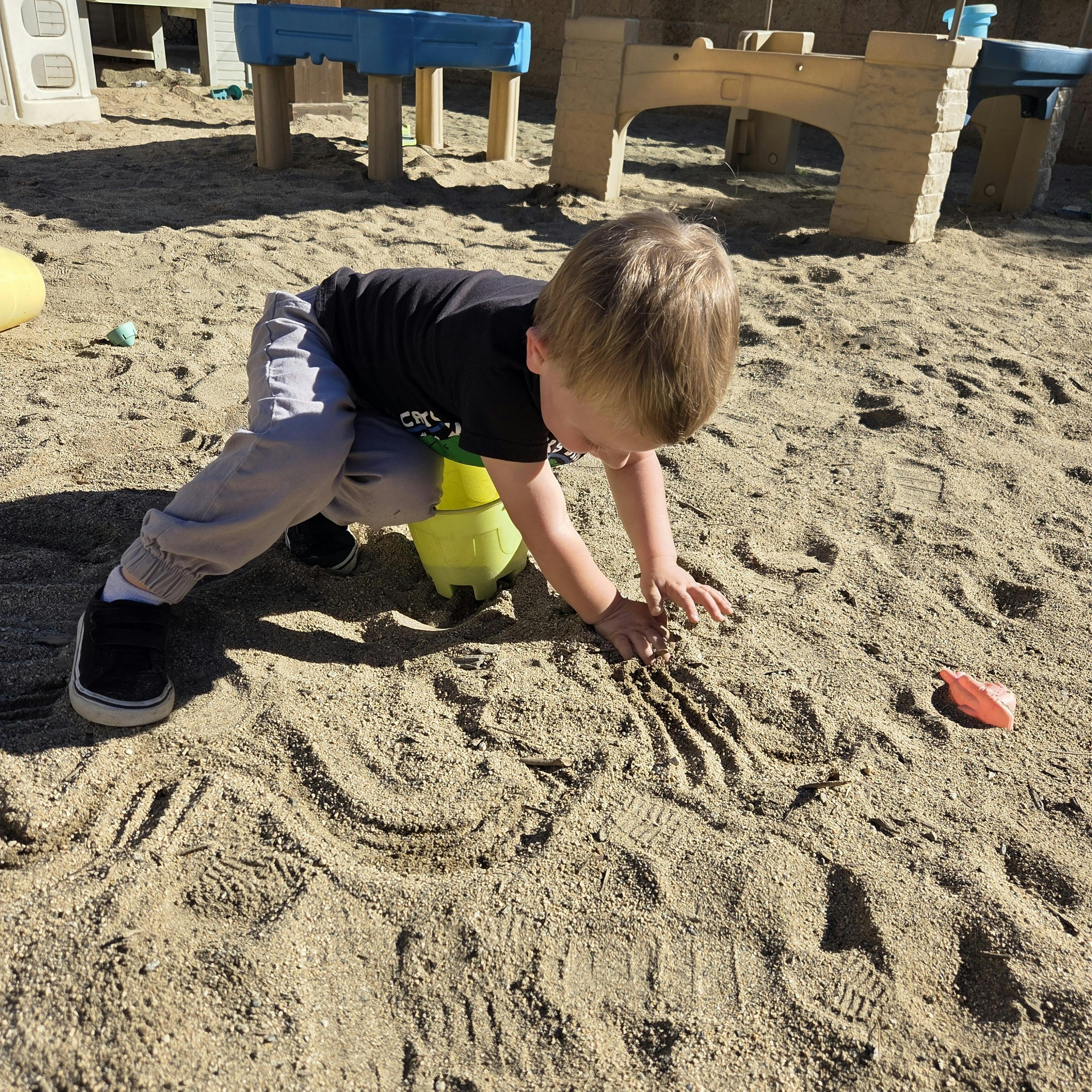 Child playing in sand, making handprints