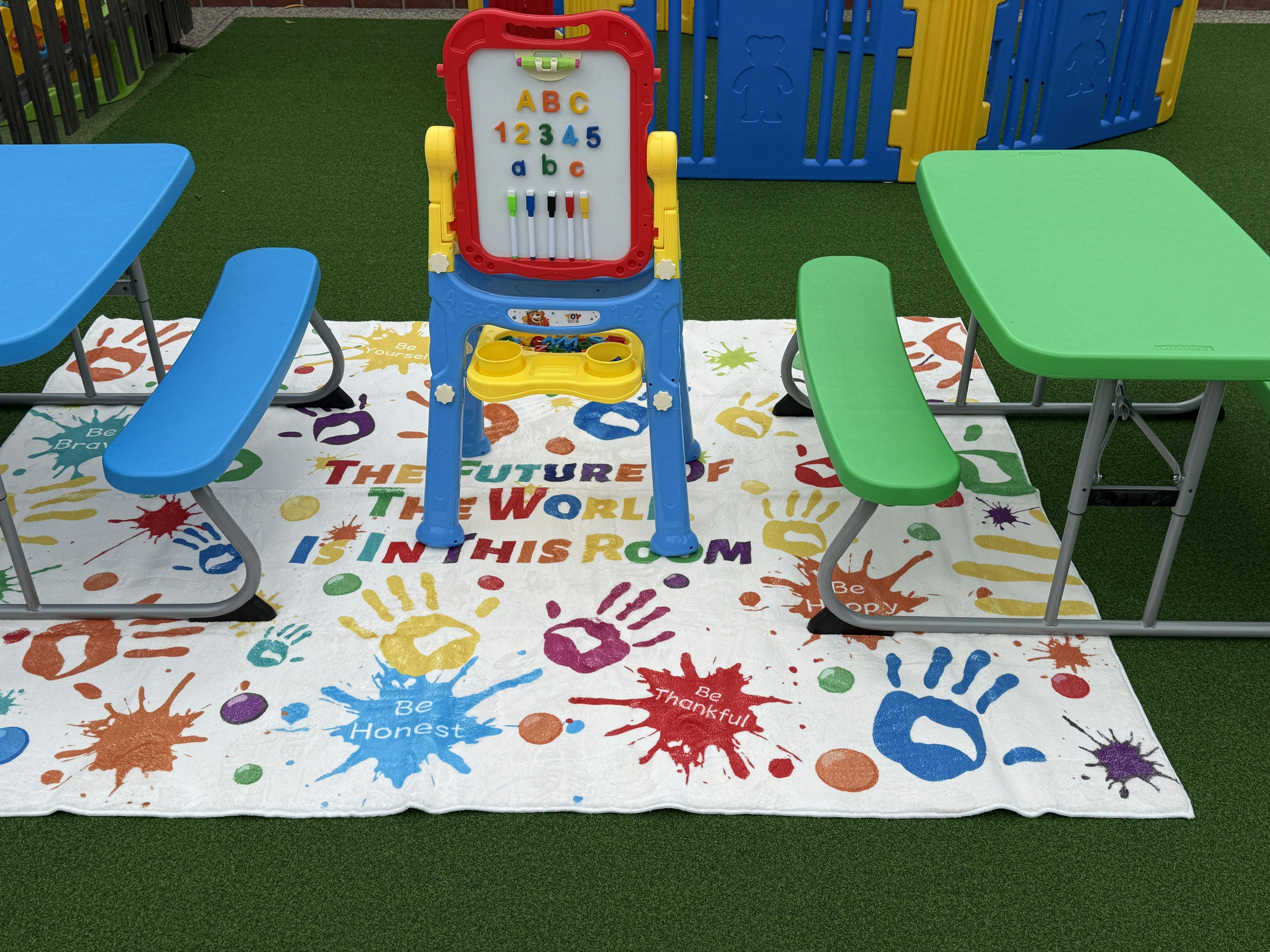 Children's play area with tables, benches, and an easel on a colorful mat
