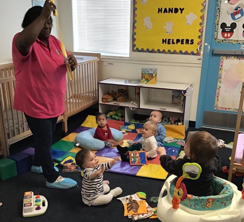 Person standing with children sitting on a mat in a room