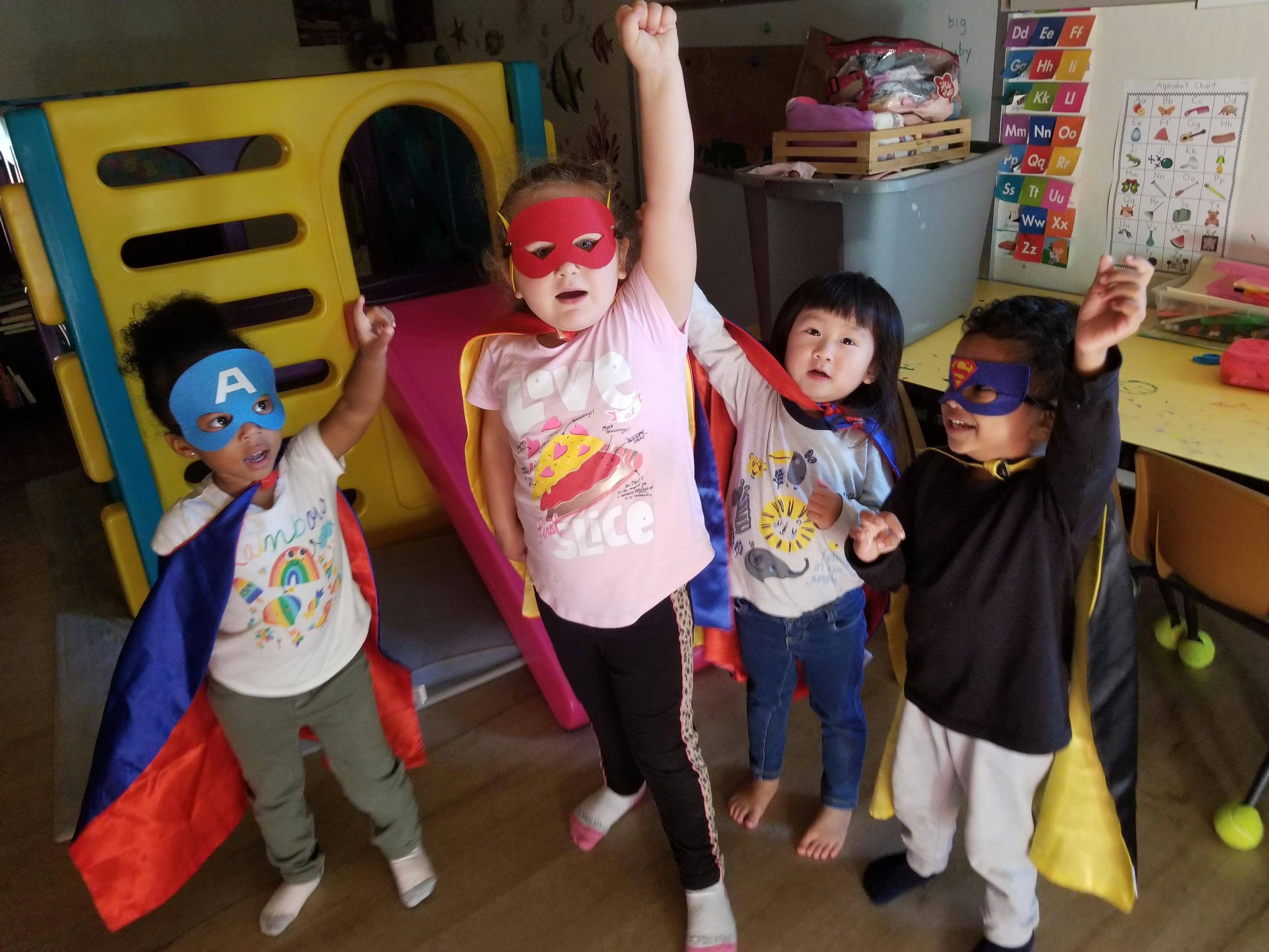 Four children in superhero masks and capes raising their fists