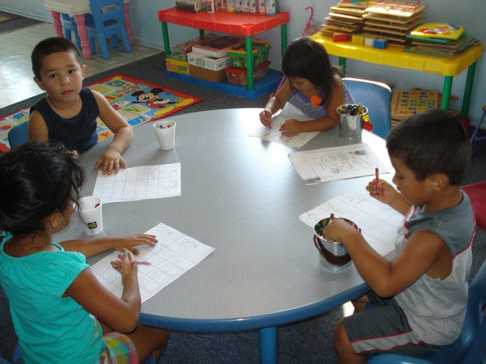 Four children drawing and writing at a round table in a classroom