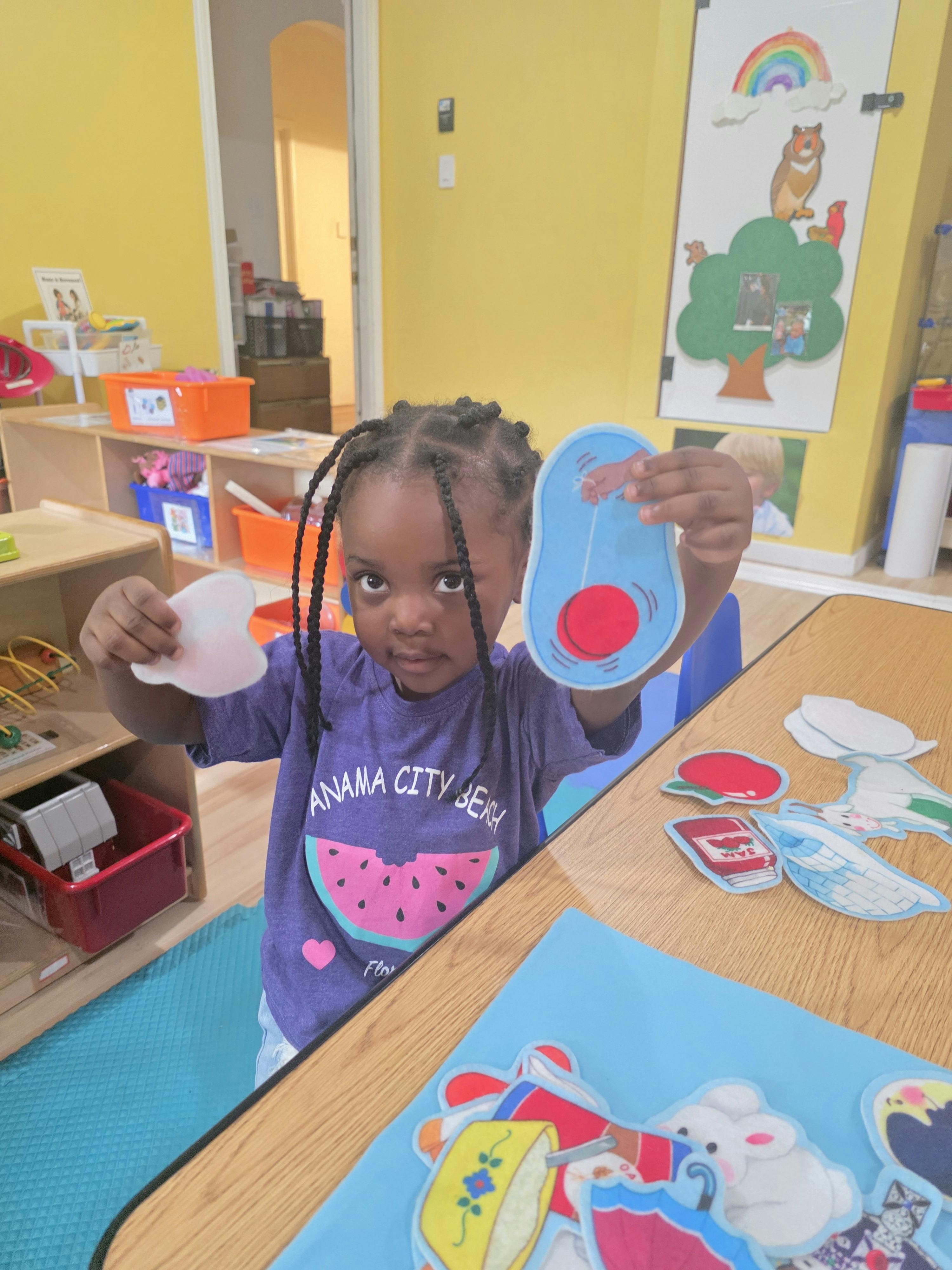 Child holding two small felt cutouts in a classroom