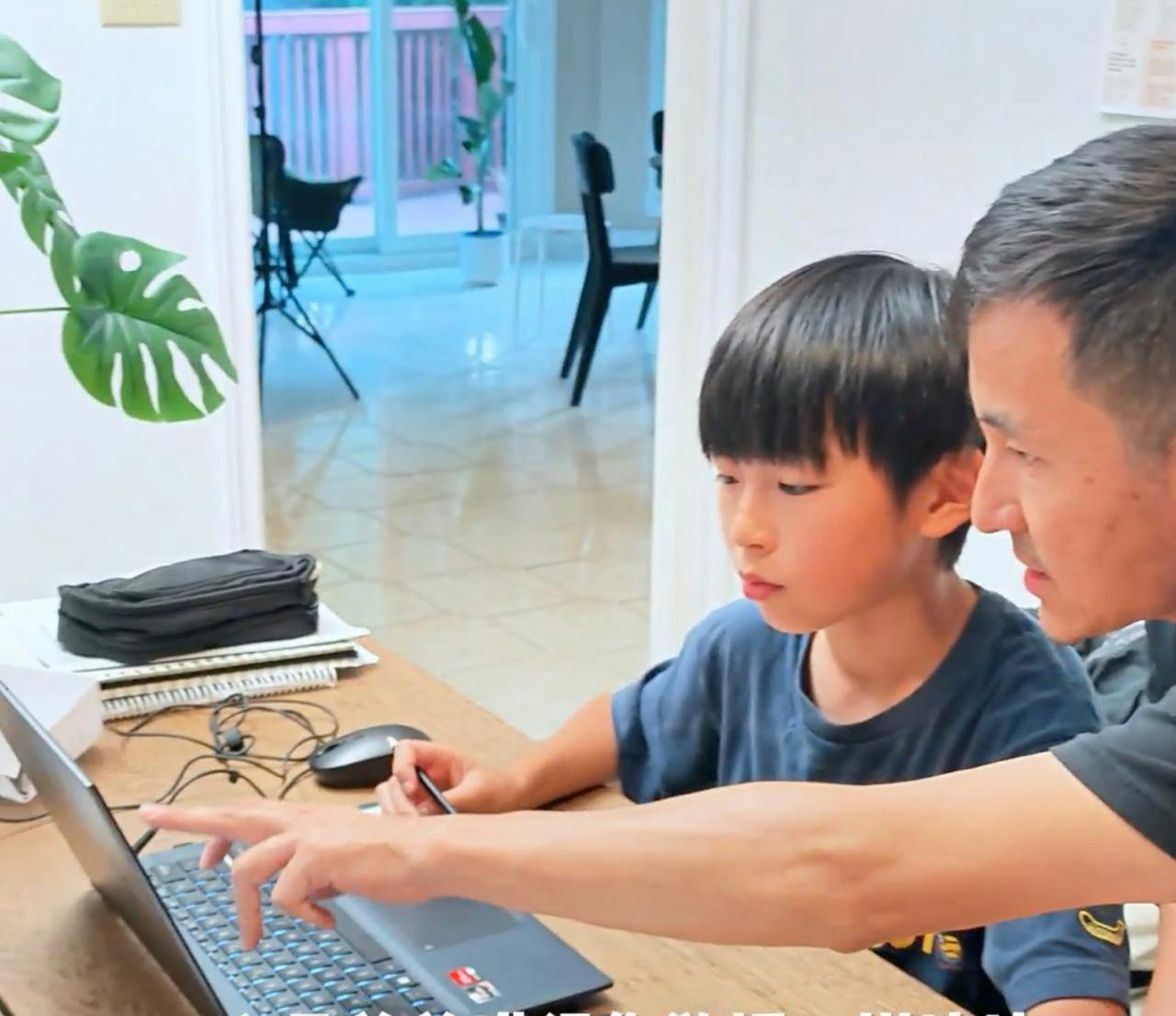 Adult pointing at a laptop screen while a child looks on at a desk