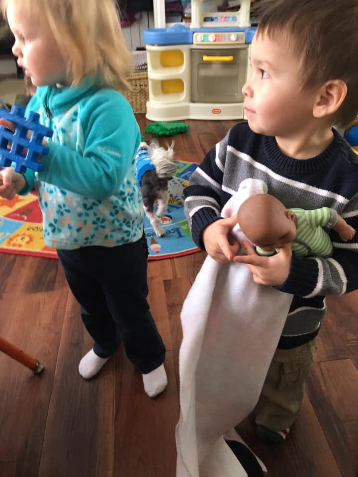 Child holding a blue toy, another child holding a doll