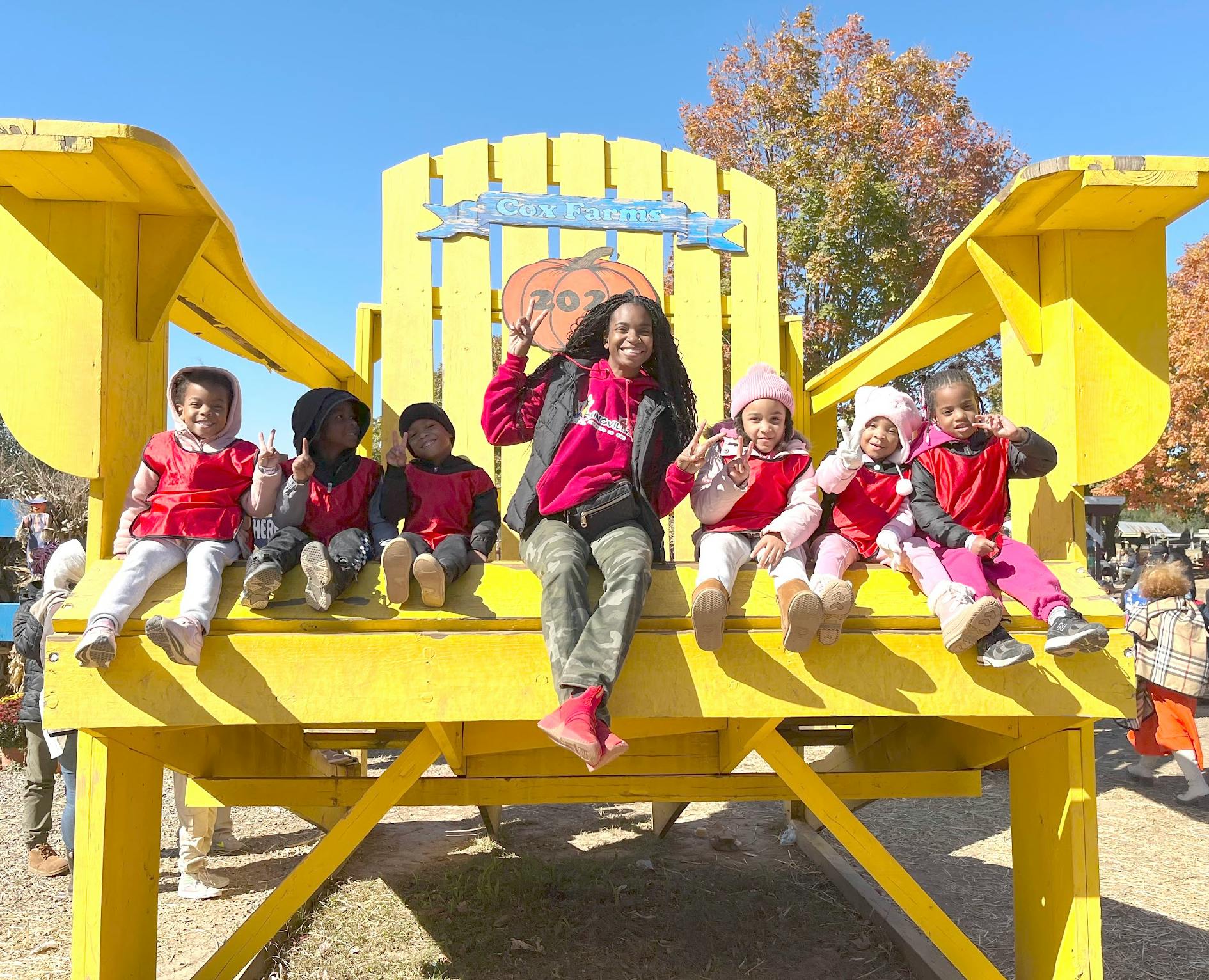 Group of children and an adult posing on an oversized yellow chair at a farm