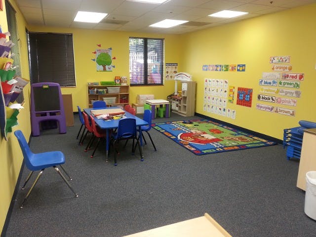 Classroom with small blue tables and chairs, colorful rug, and yellow walls