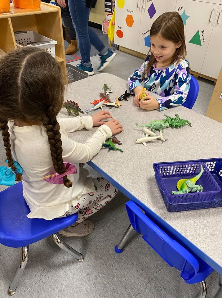Two children playing with dinosaur toys at a table