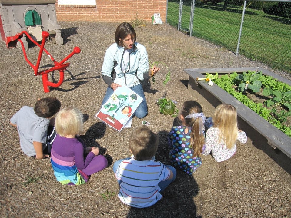 Person kneeling with children around a garden bed