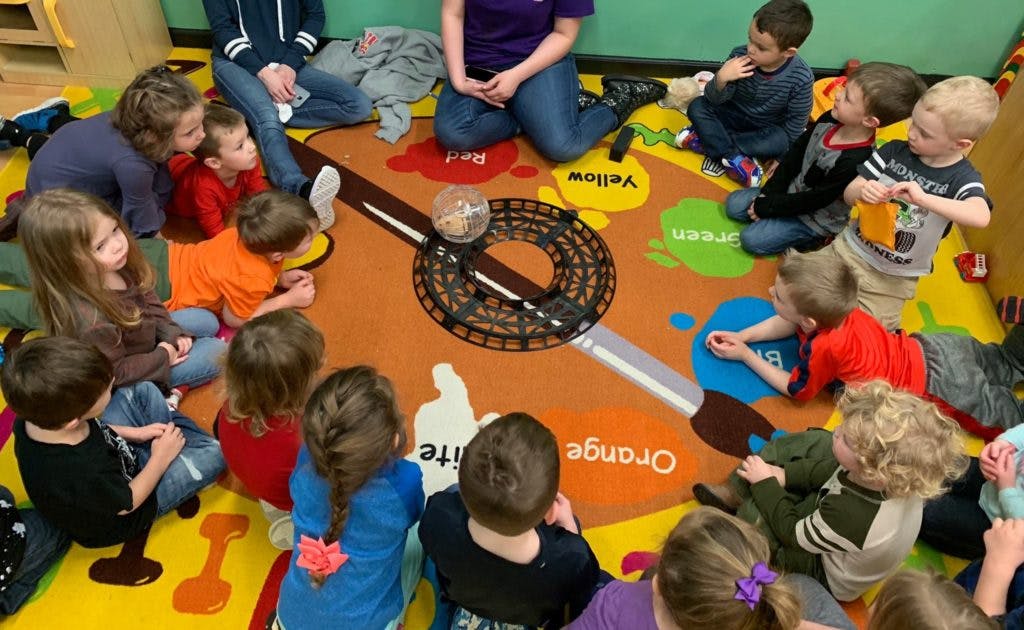 Adults and children sitting on a colorful rug in a classroom