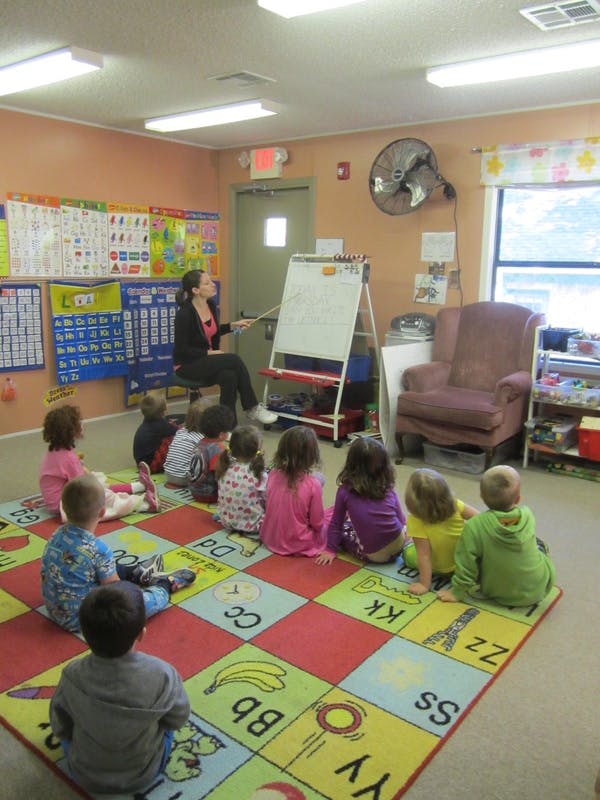 Person teaching children sitting on a colorful alphabet rug in a classroom