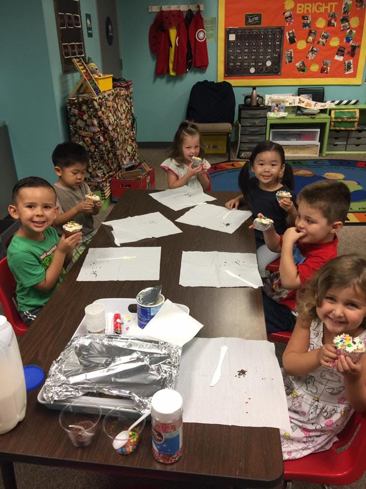 Children sitting at a table eating cupcakes in a classroom