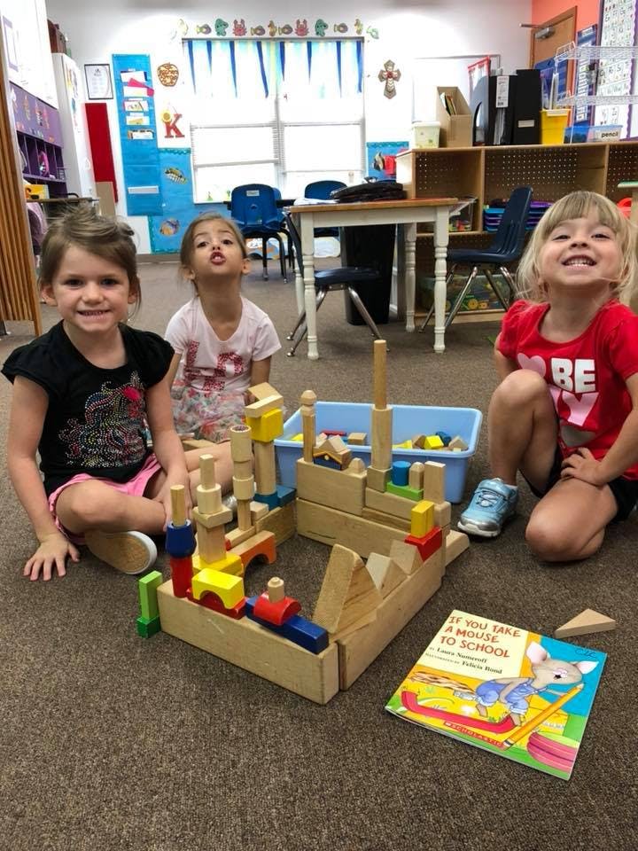 Three children sitting on the floor with wooden blocks and a book