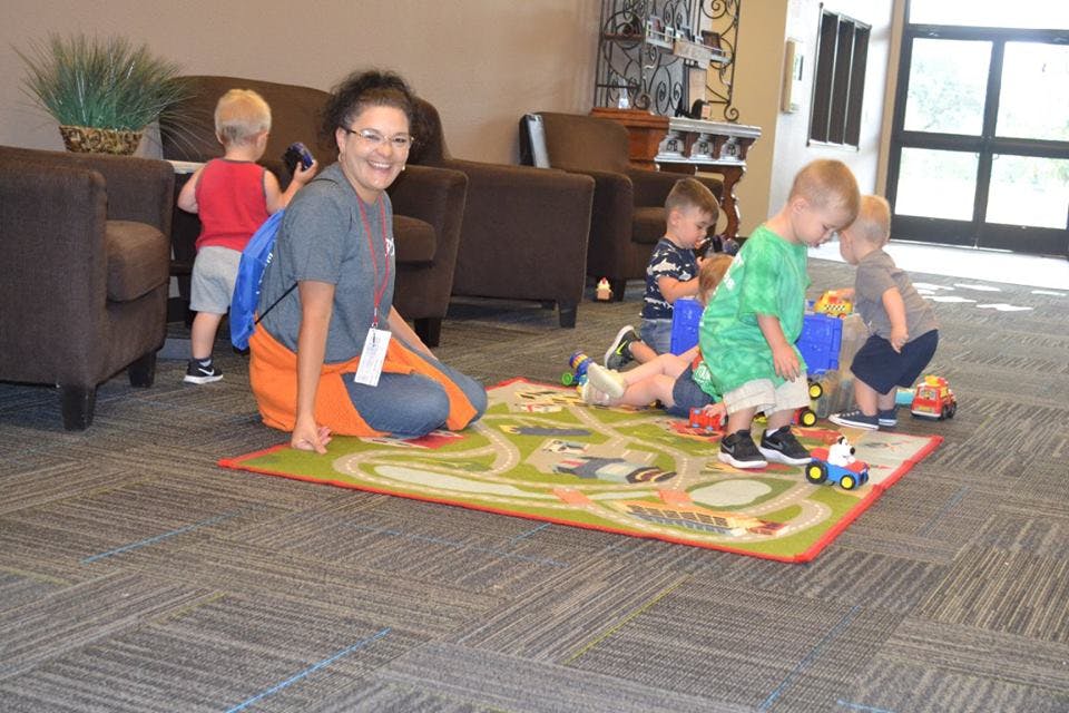 Person kneeling on a rug with several children playing with toys