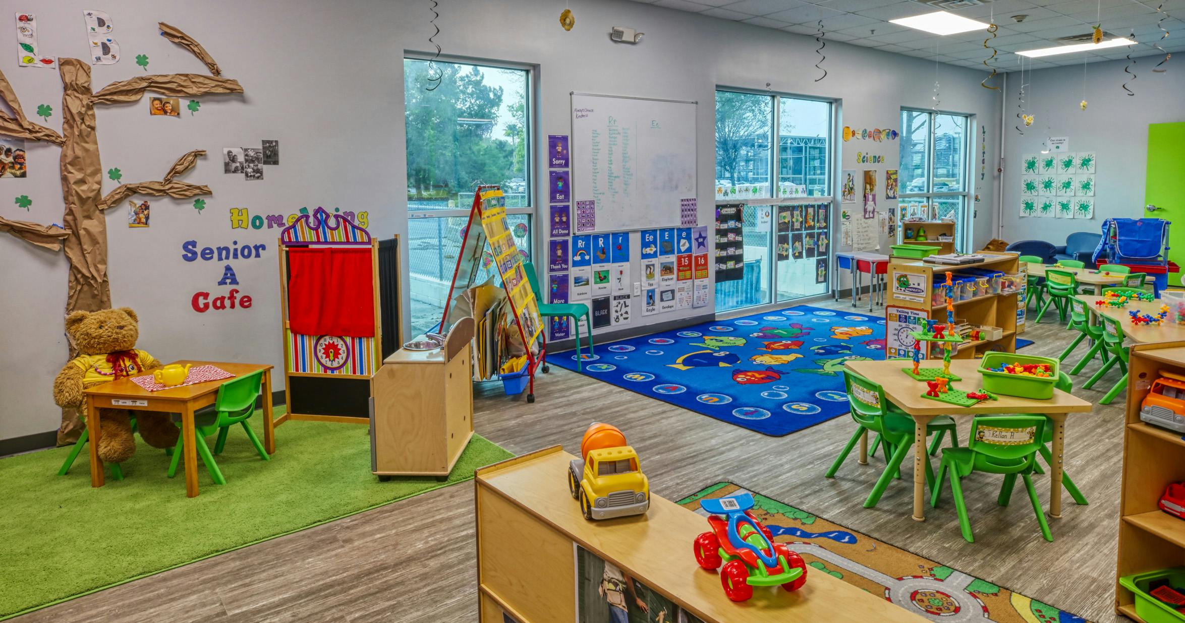 Classroom with play areas including a teddy bear at a table, puppet stage, and toys