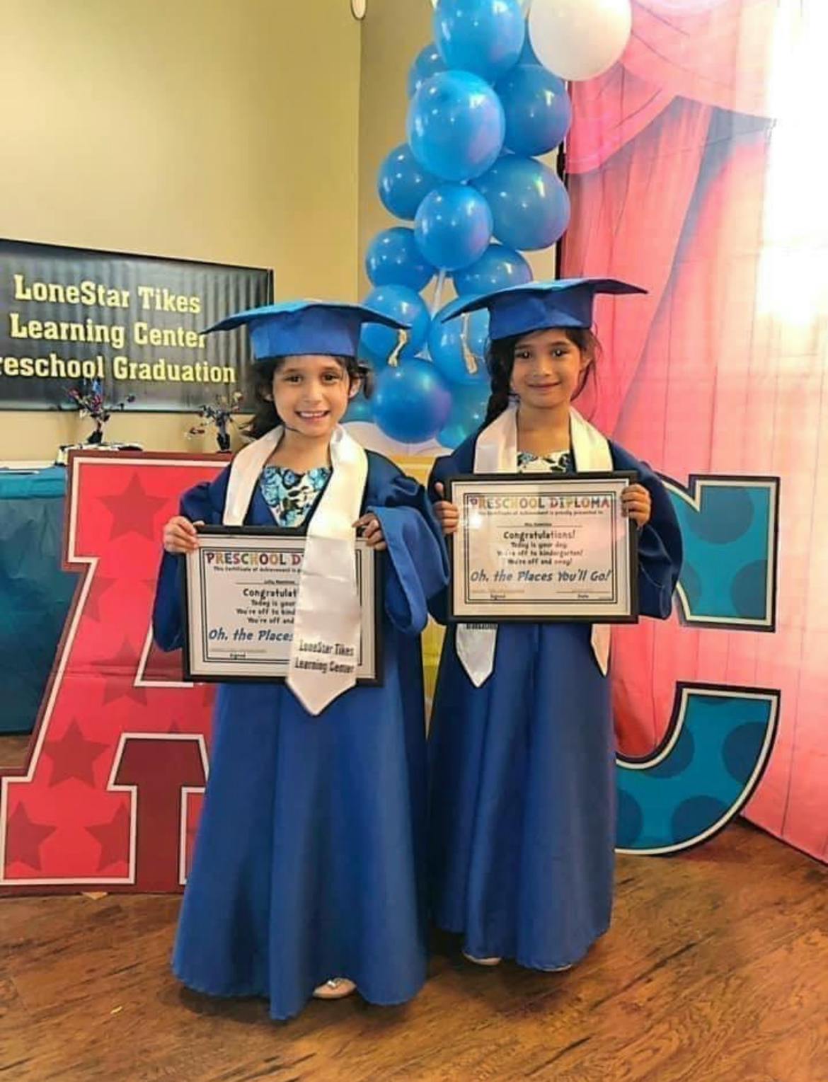 Two children in graduation caps and gowns holding diplomas
