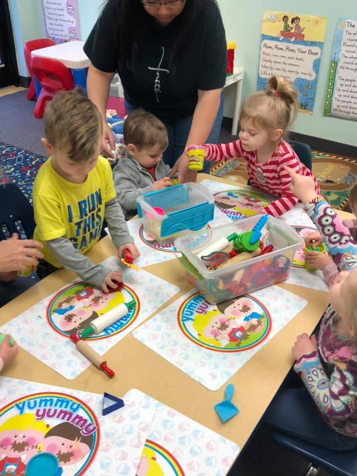 Adult supervising children playing with modeling clay at a table