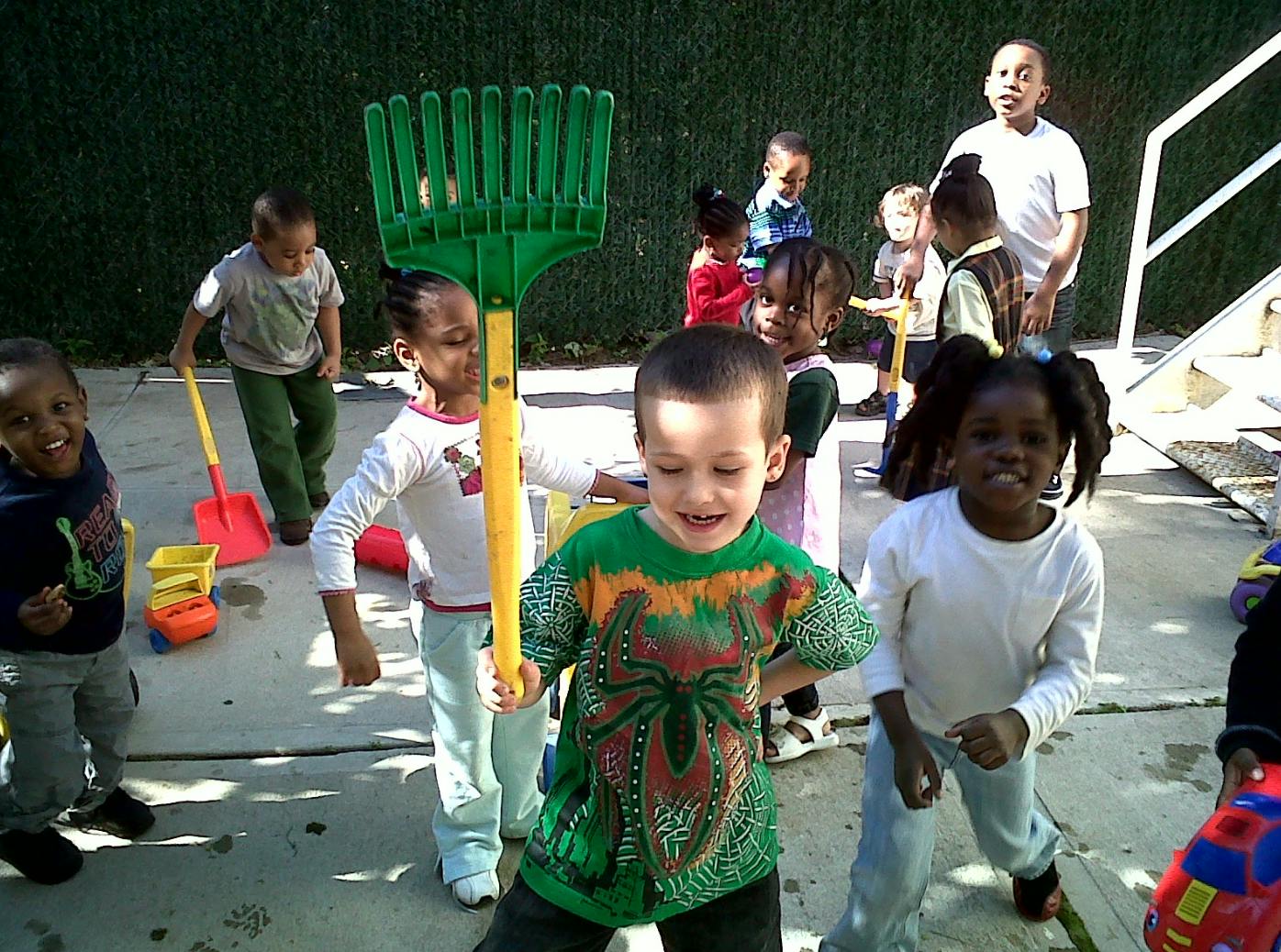Children playing outdoors with a large green rake and other toys