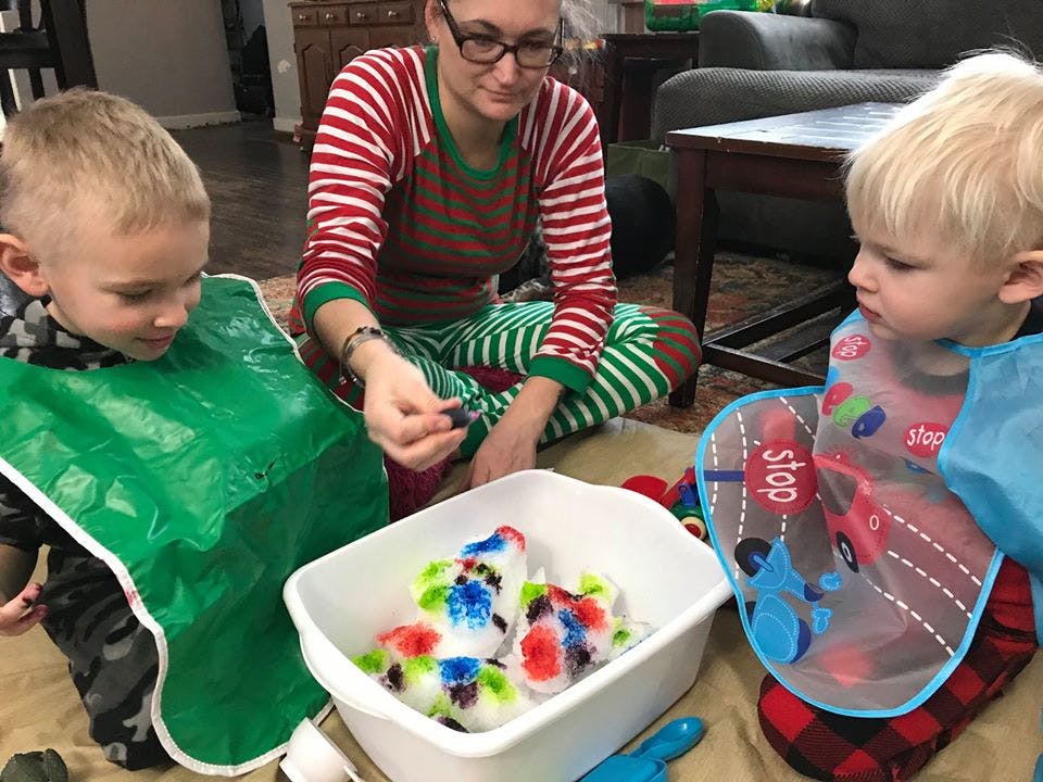Person and two children playing with colorful ice in a tub