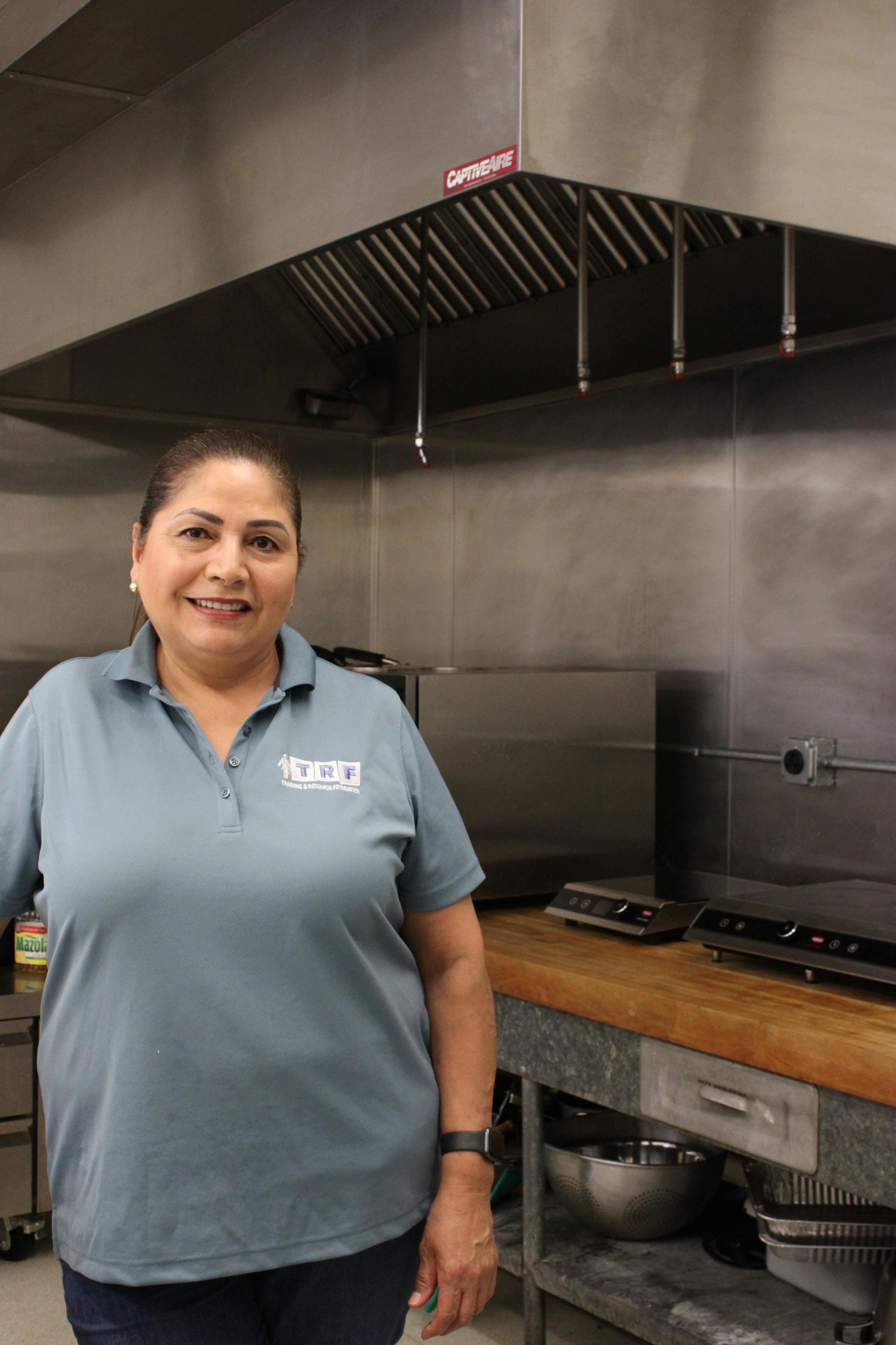 Person in a blue polo shirt with a logo, smiling in a kitchen