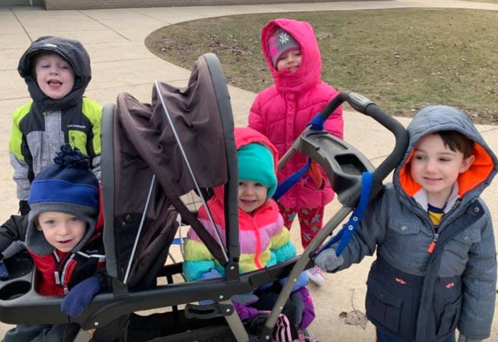 Four children in winter coats and hats around a double stroller