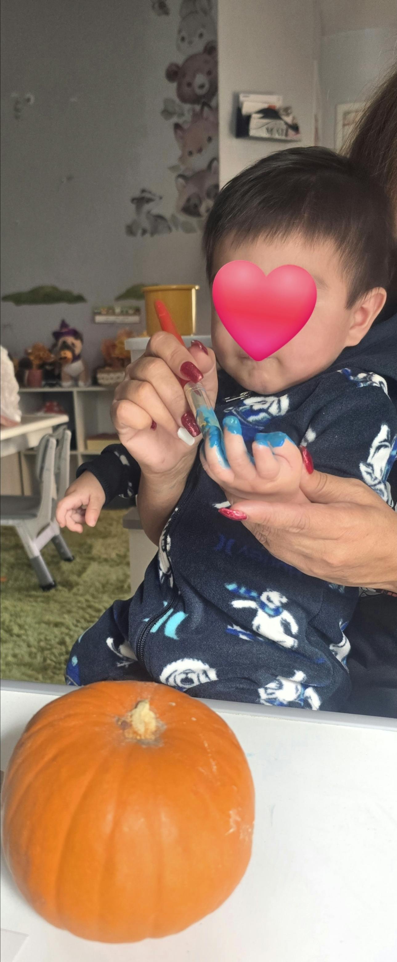 Person holding a child who is painting a pumpkin