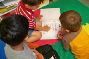Three children looking at a book on the floor