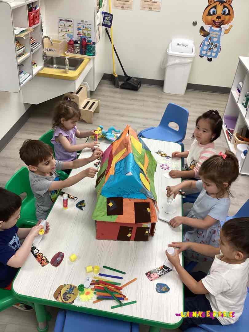 Children sitting around a table decorating a large colorful house