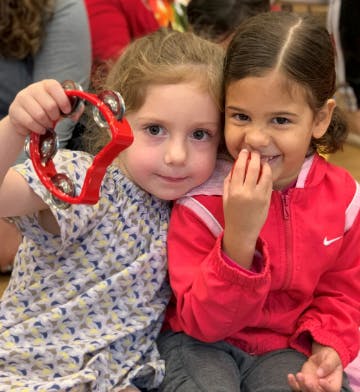 Two children sitting together, one holding a red tambourine