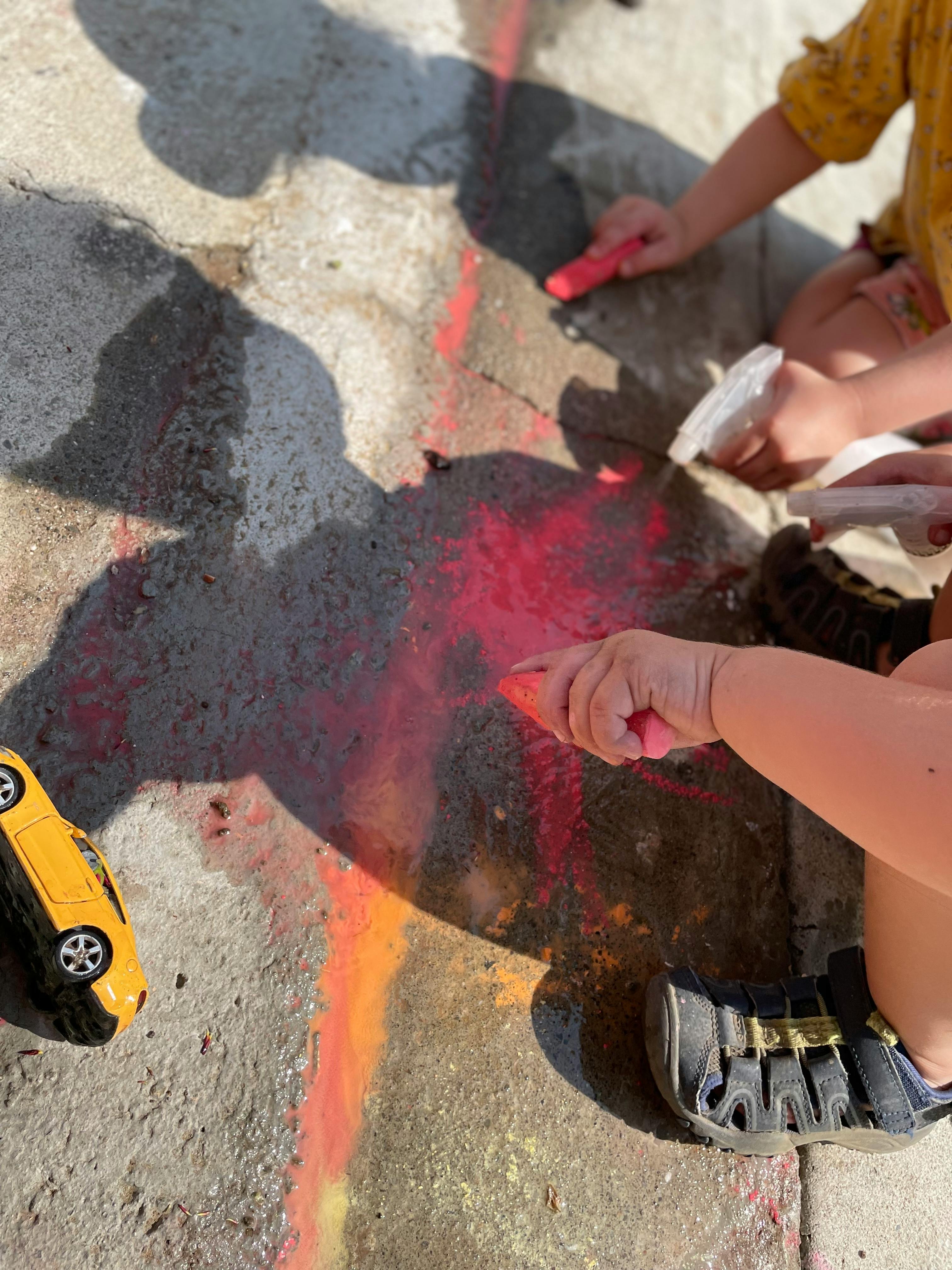 Child's hands drawing with chalk on pavement