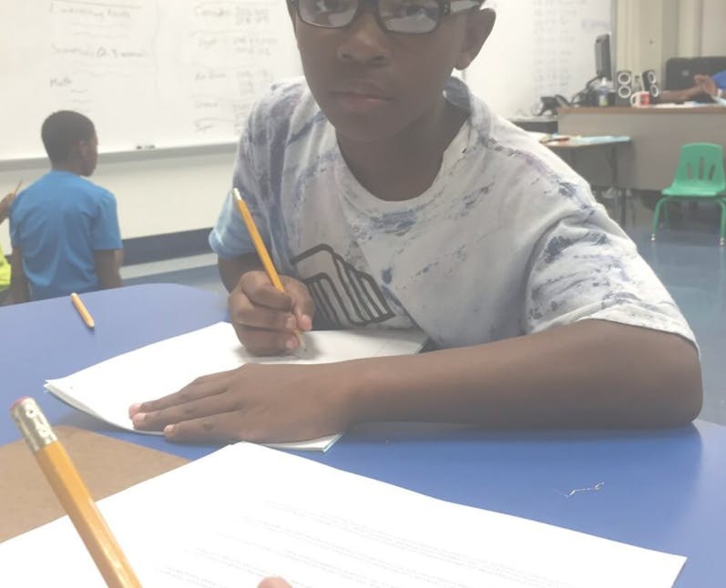 Child in glasses writing with a pencil in a classroom