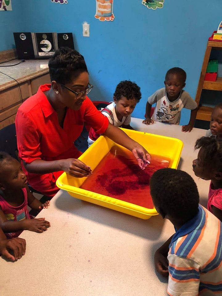 Person in red shirt showing children a tray with red liquid
