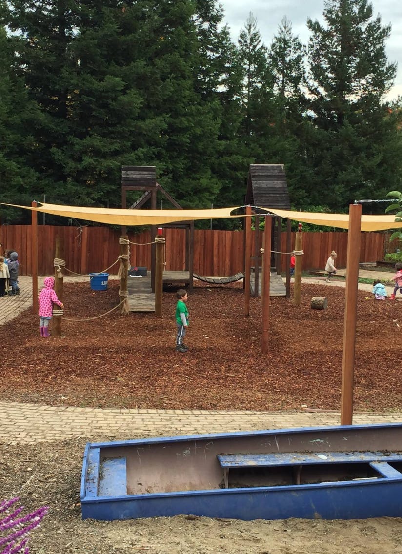 Children playing on a playground with wood chips and a shade sail