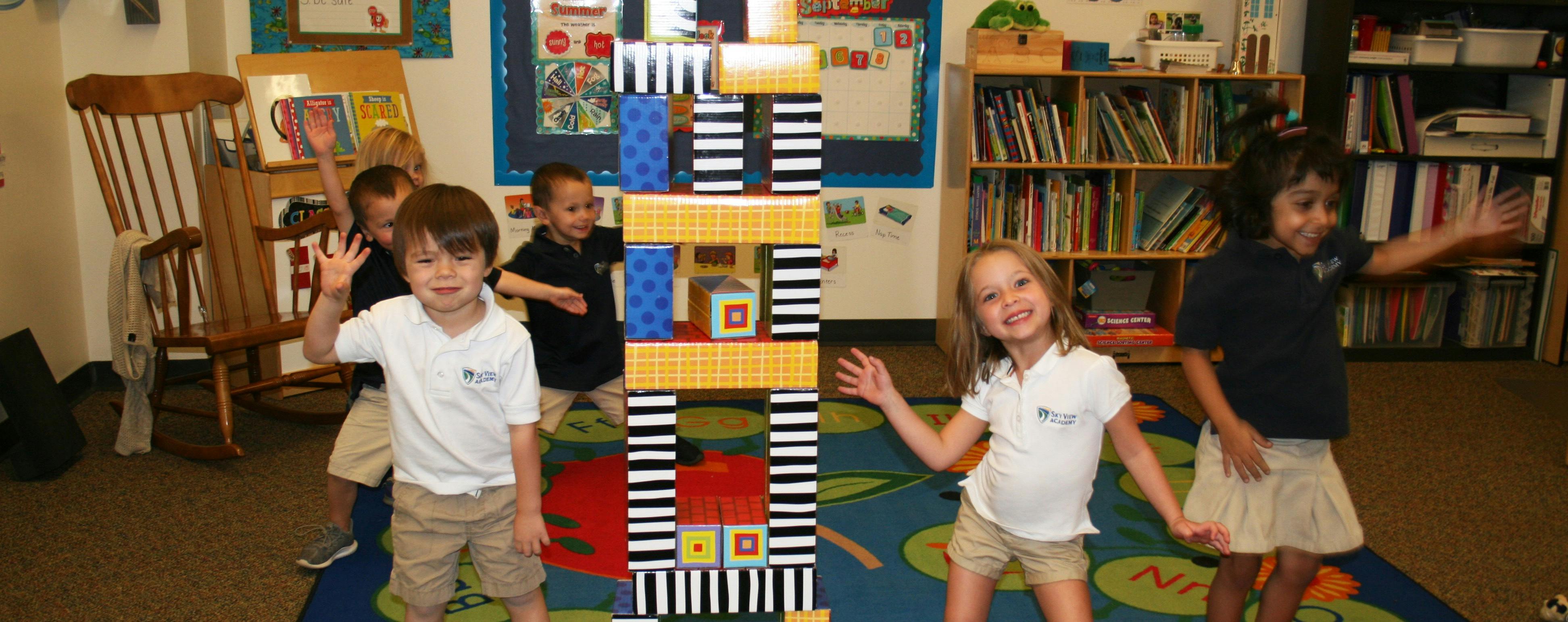Children standing around a tall block tower in a classroom