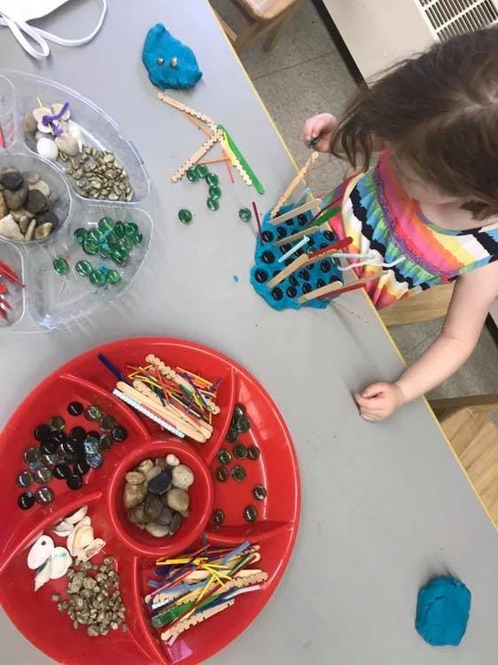 Child playing with blue playdough and craft sticks at a table