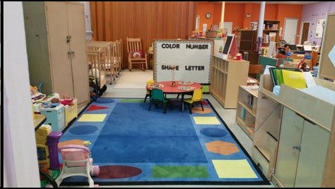 Playroom with a blue rug, small table and chairs, and cribs