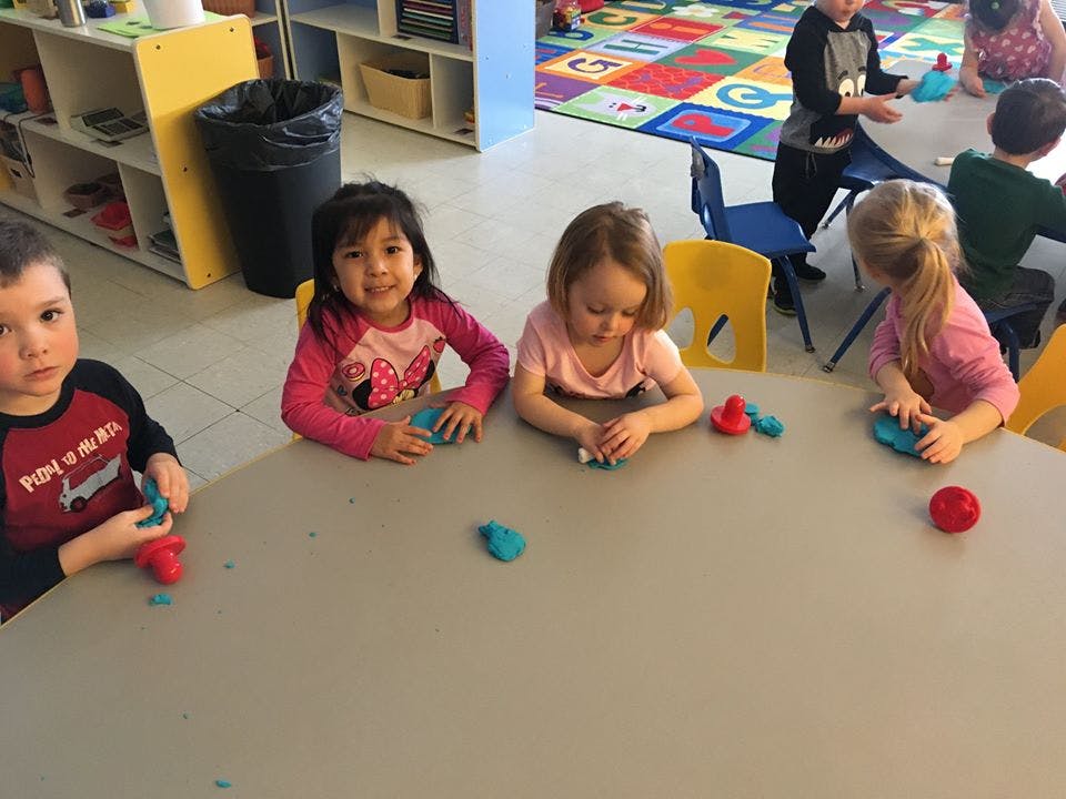 Children playing with modeling clay at a table in a classroom