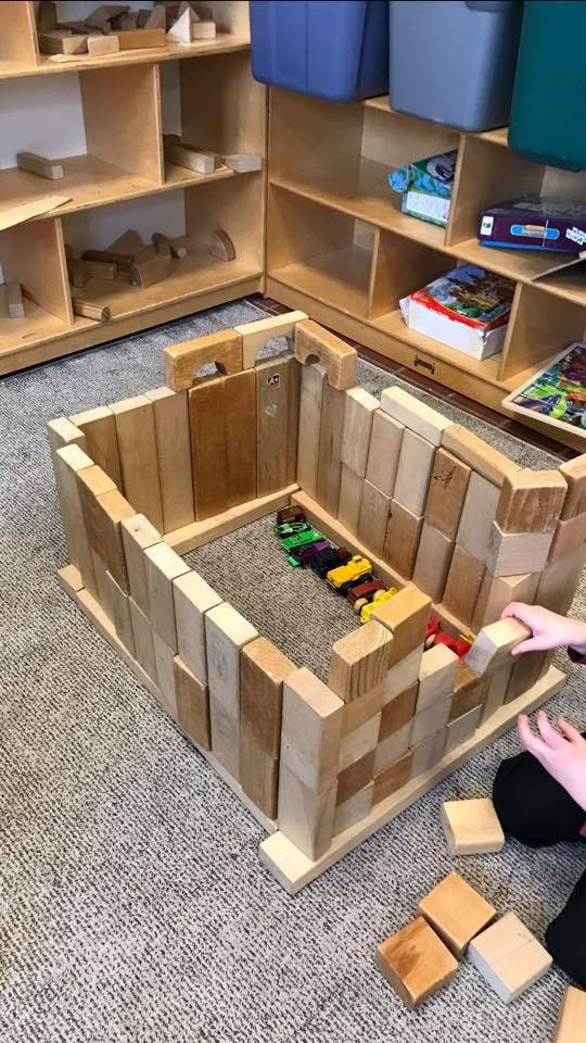 Person building a structure with wooden blocks on a carpeted floor
