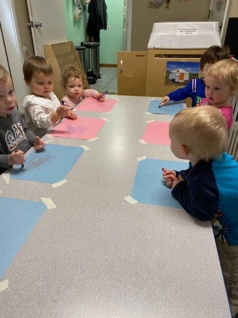 Children sitting at a table with paper and crayons