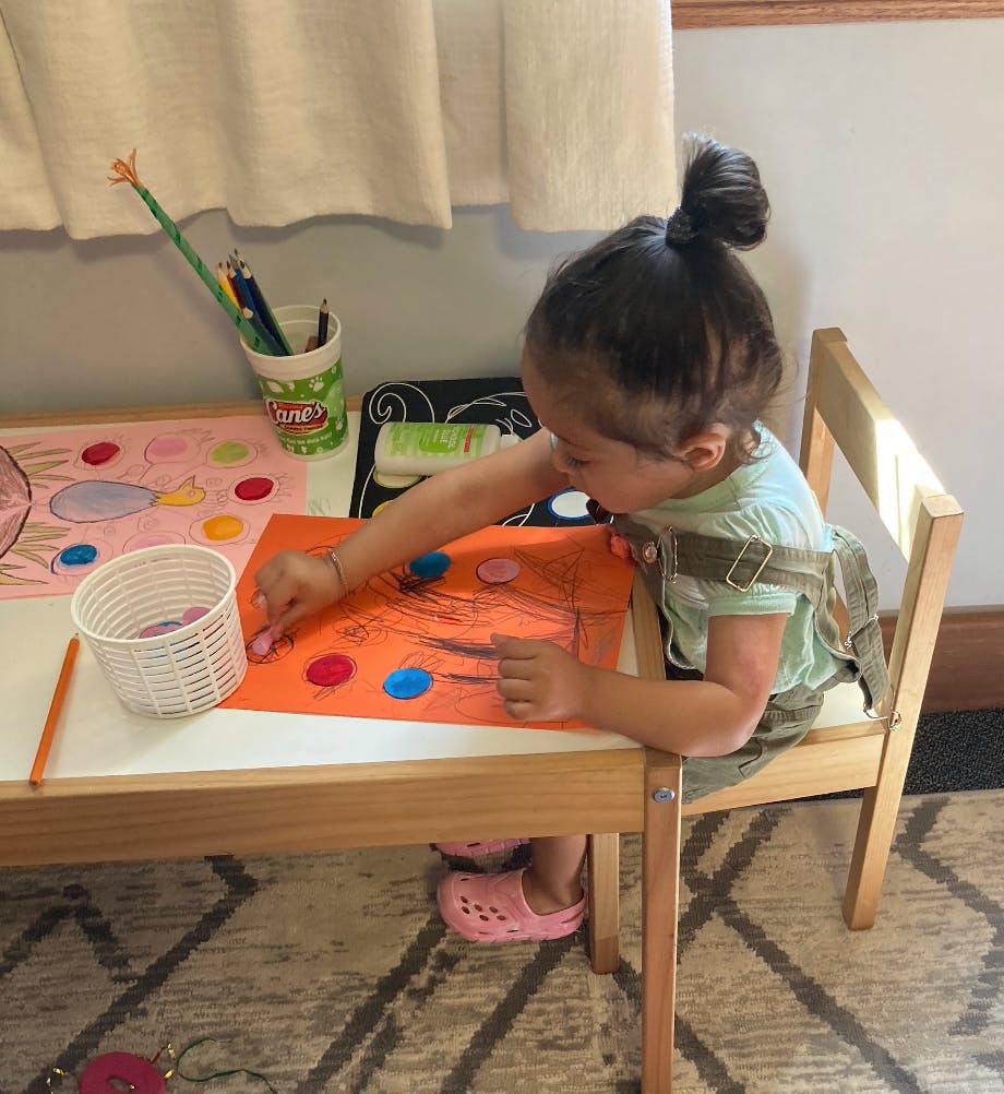 Child sitting at a table and drawing on orange paper