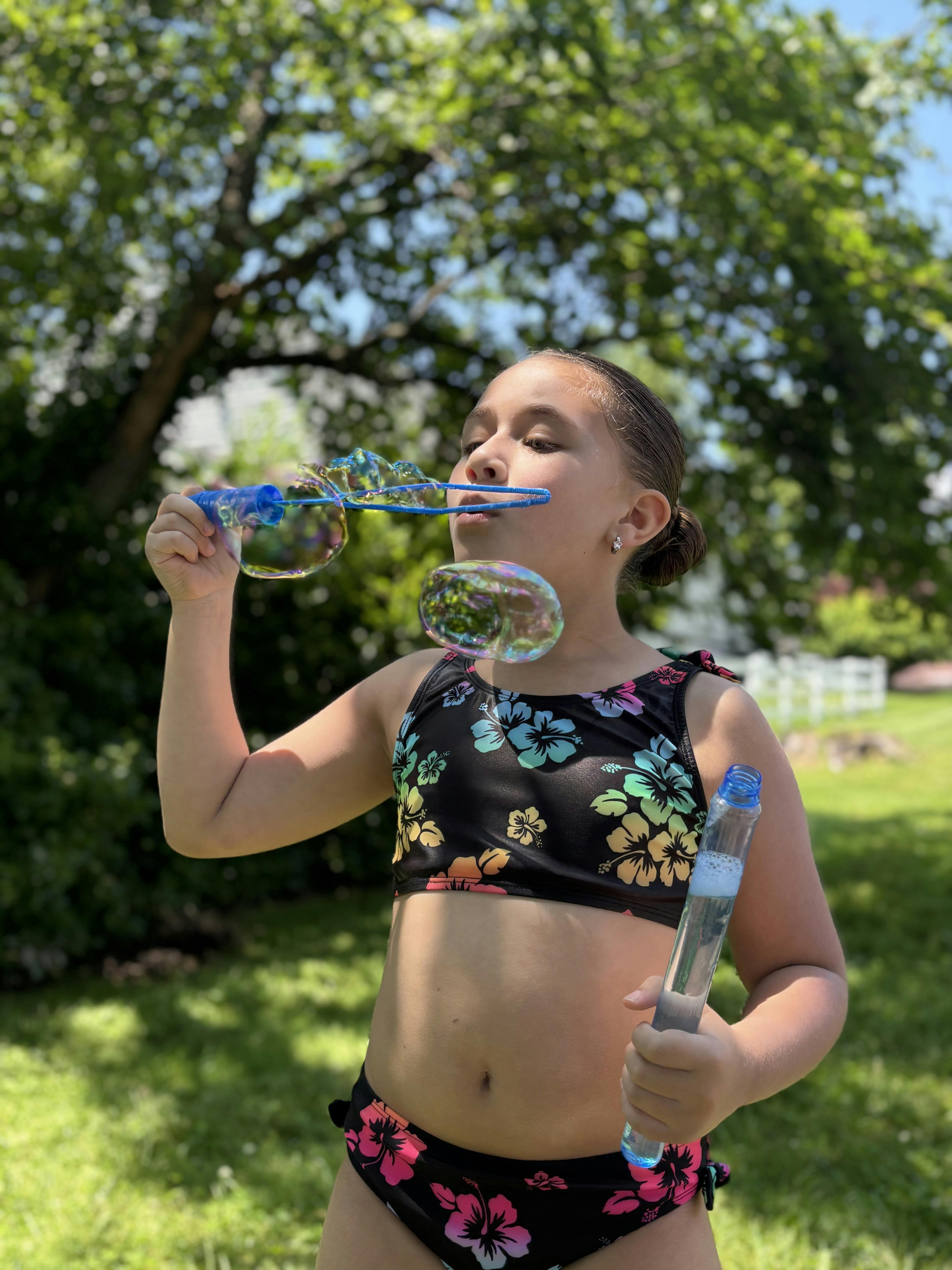 Child in a swimsuit blowing bubbles outdoors