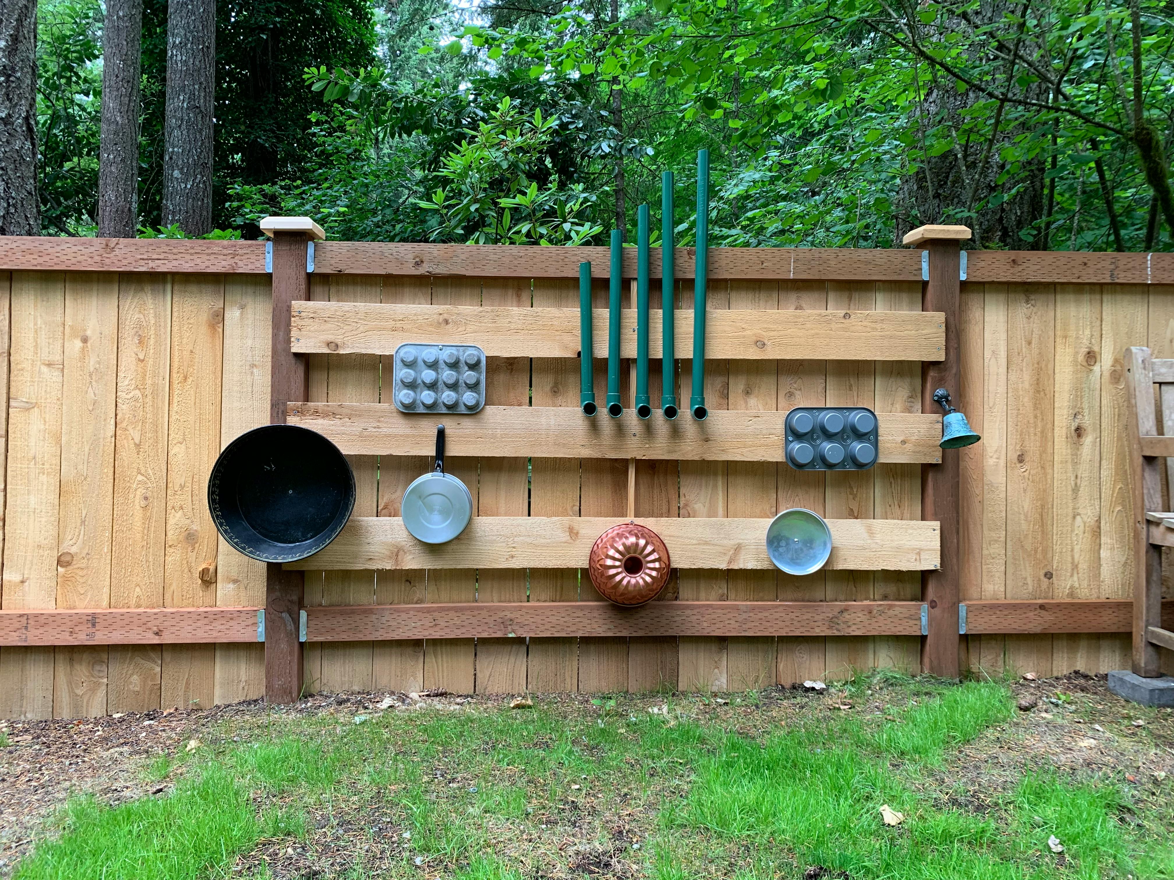Outdoor fence with various kitchen items and green pipes attached