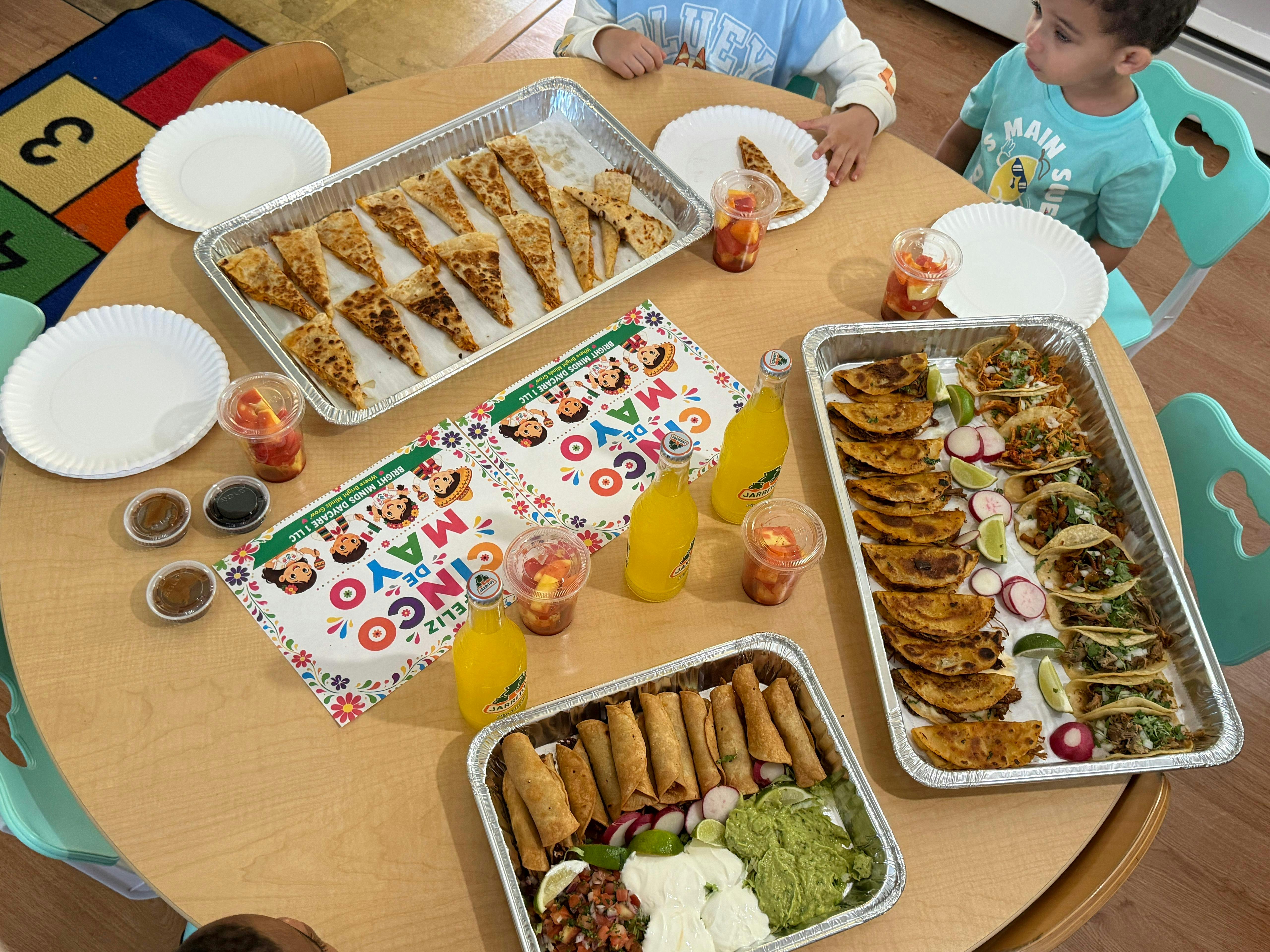 Children sitting around a table with quesadillas, tacos, and drinks