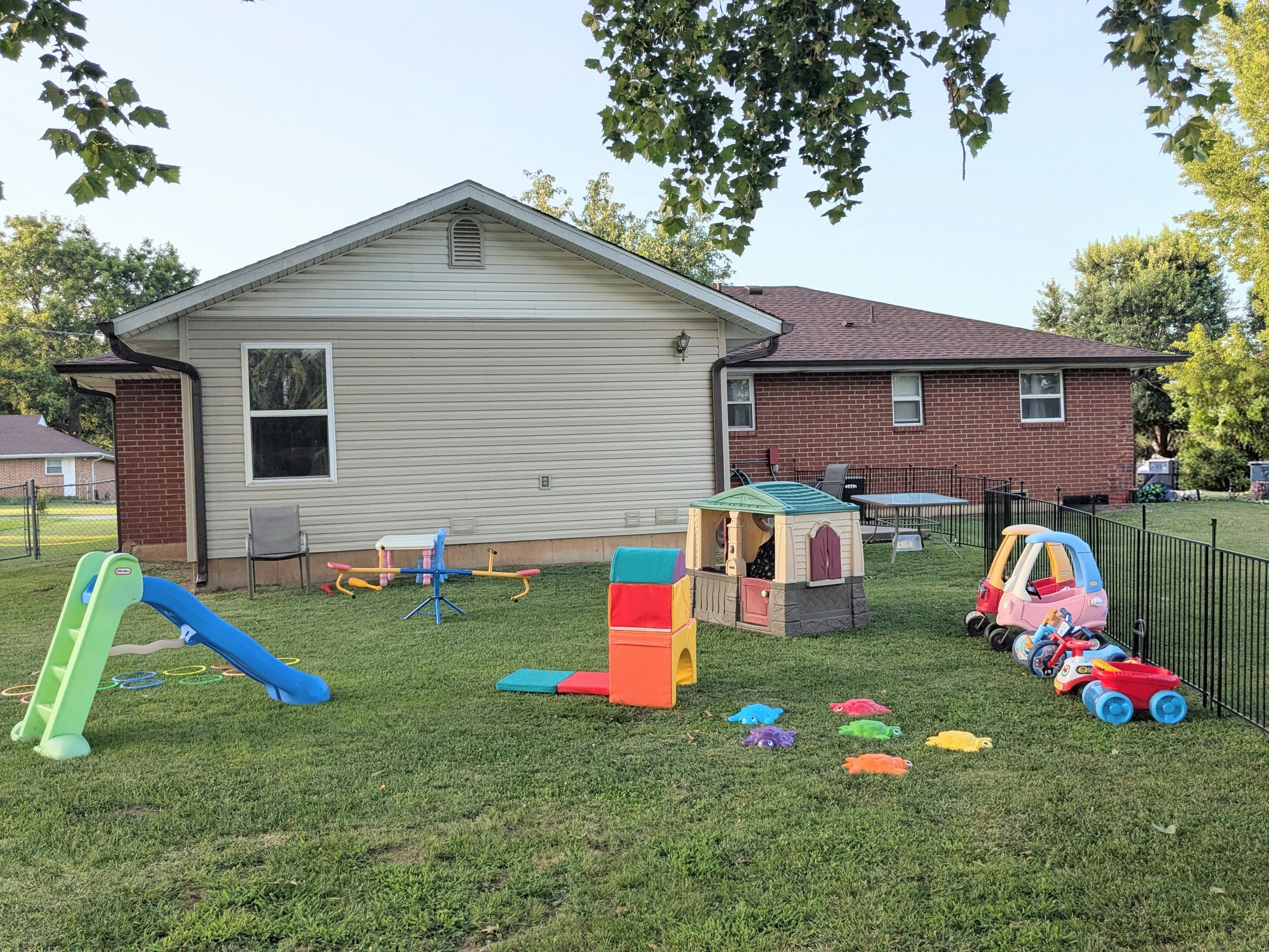 Playground equipment and toy cars on a grassy lawn in front of a house