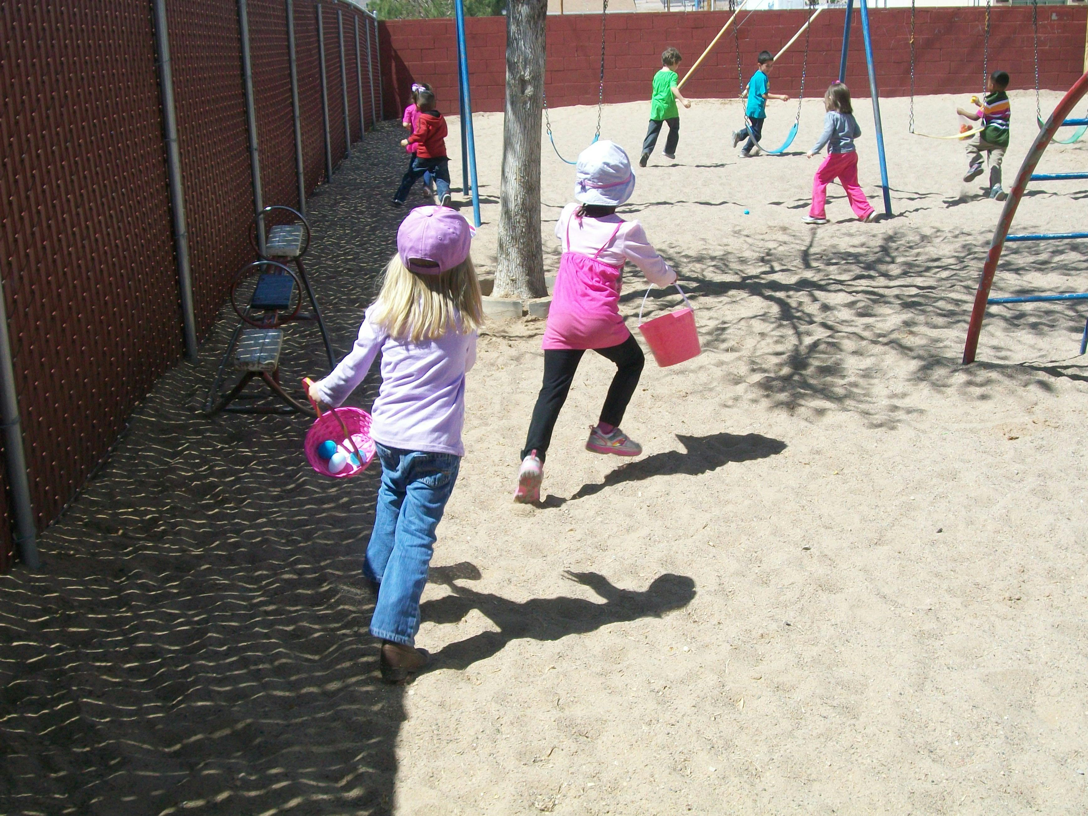 Children playing in a sandy area with a fence and playground equipment